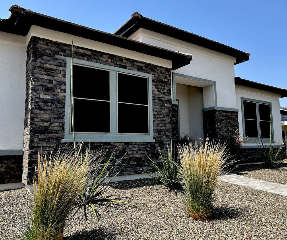 Modern house with stone accents, large windows, and desert landscaping under a blue sky.