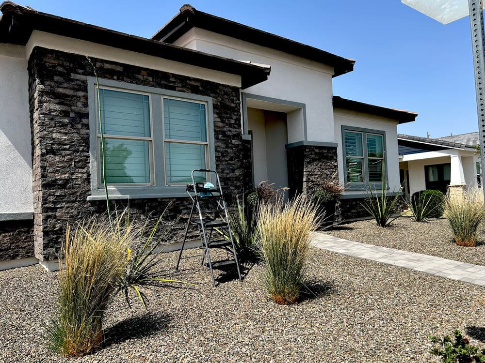 Modern house with stone accents, green landscaping, and a ladder in the front yard.