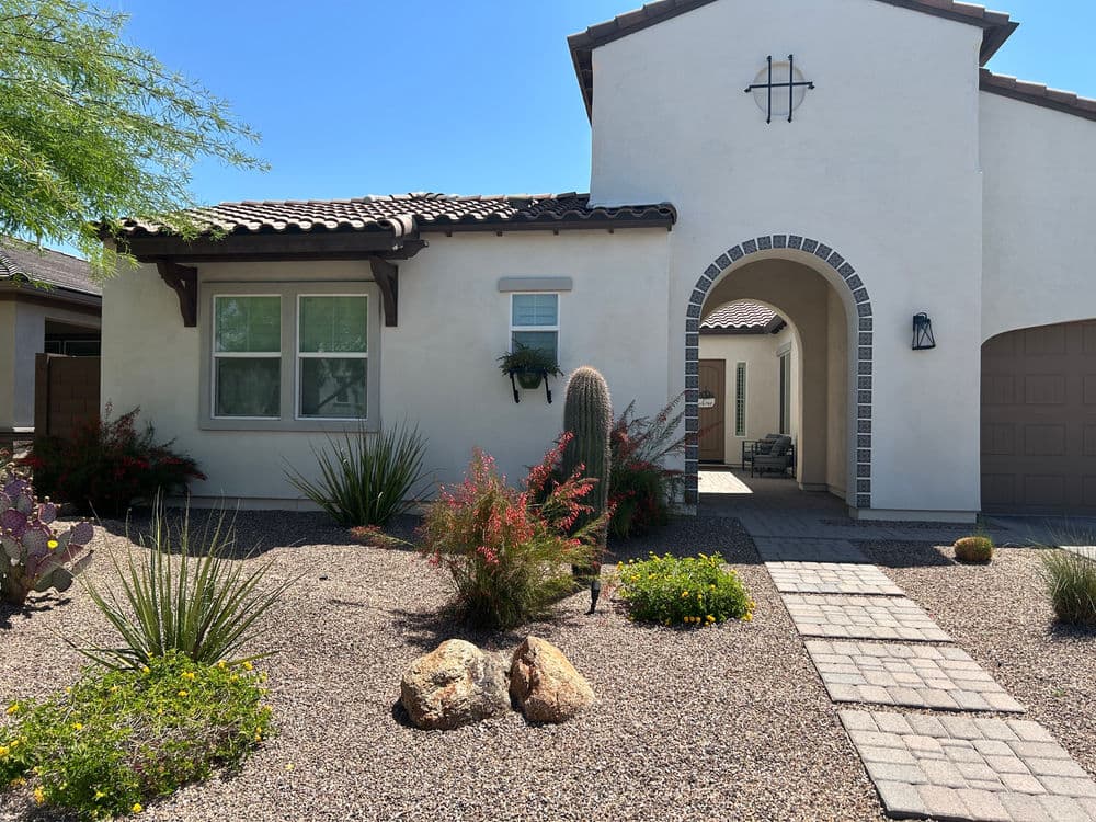 Desert-style home with arched entry, landscaping, and cactus in front yard.