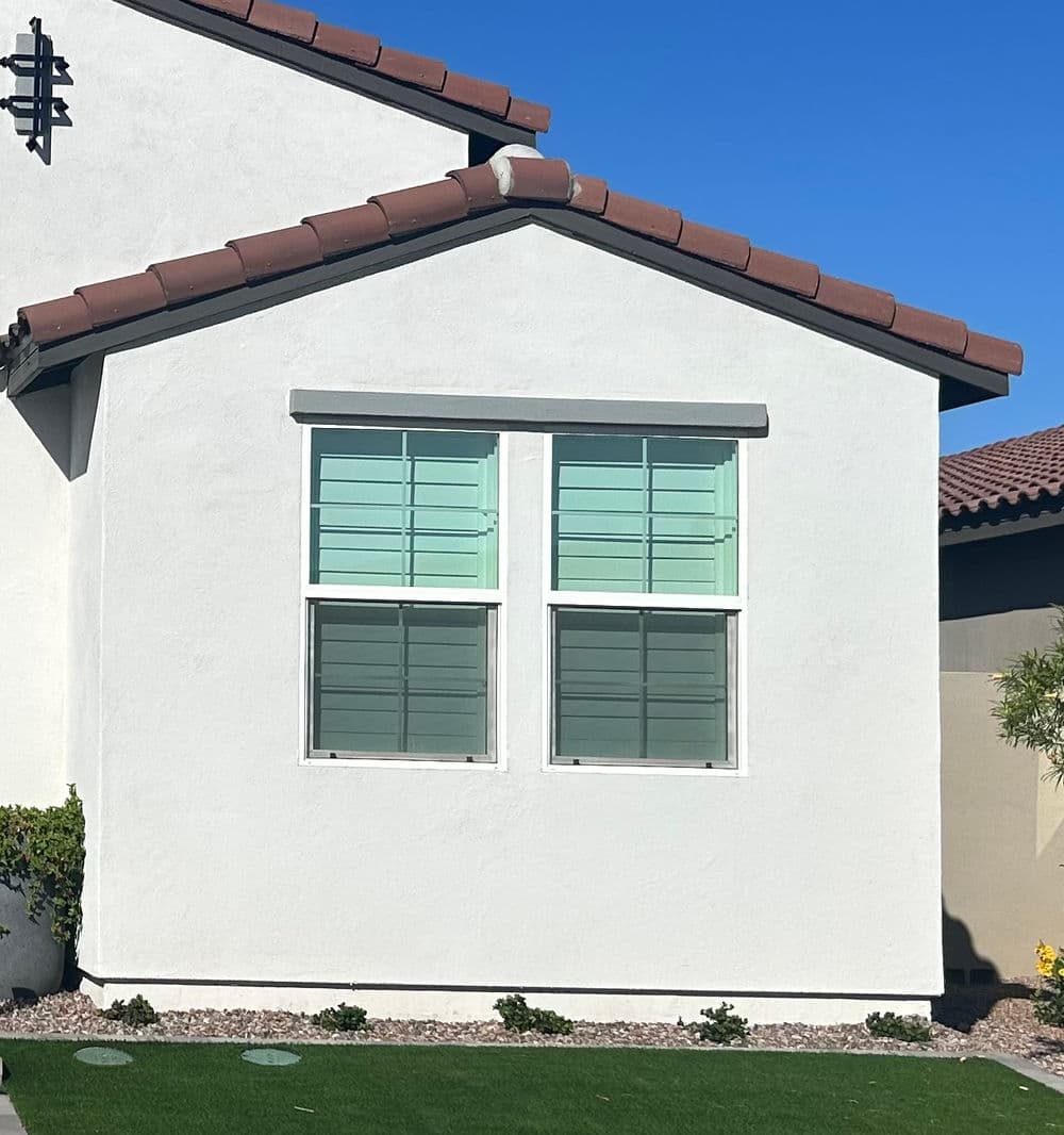 White house exterior featuring two green-shuttered windows and a tiled roof.