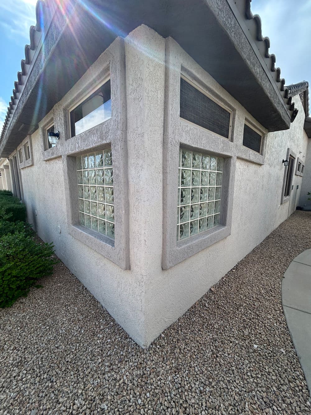 Corner view of a house featuring decorative glass block windows and textured stucco exterior.